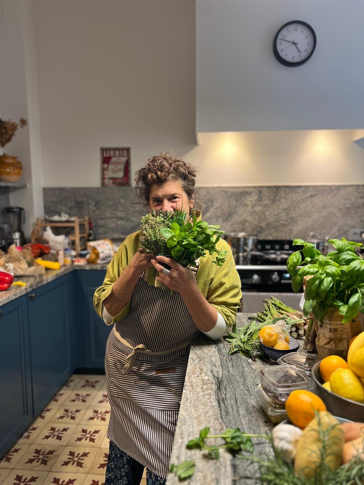Chef Lisa Esposito in an apron holding a bunch of fresh herbs to her face in the kitchen