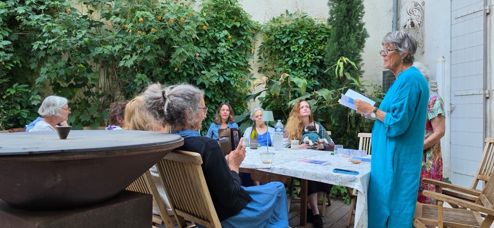 Ros standing to read to a group of writers seated around a table in the garden