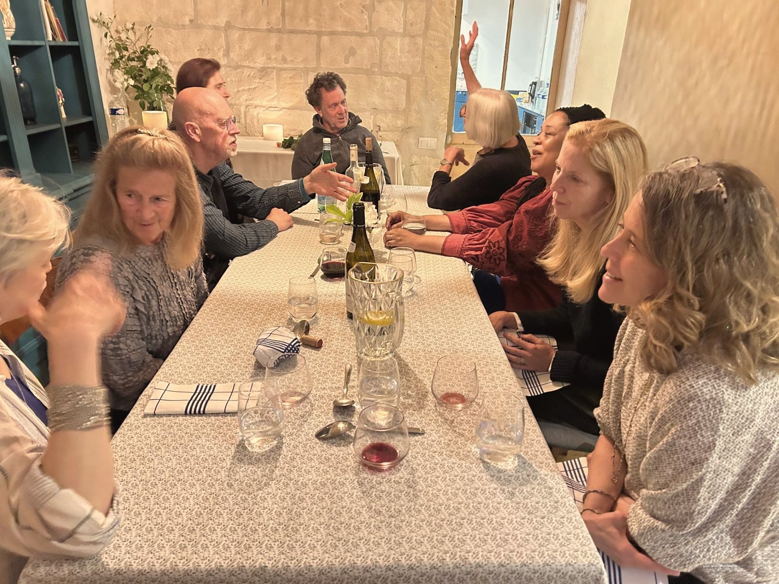 Writers talking and laughing around a long table with a patterned cloth, glasses and bottles
