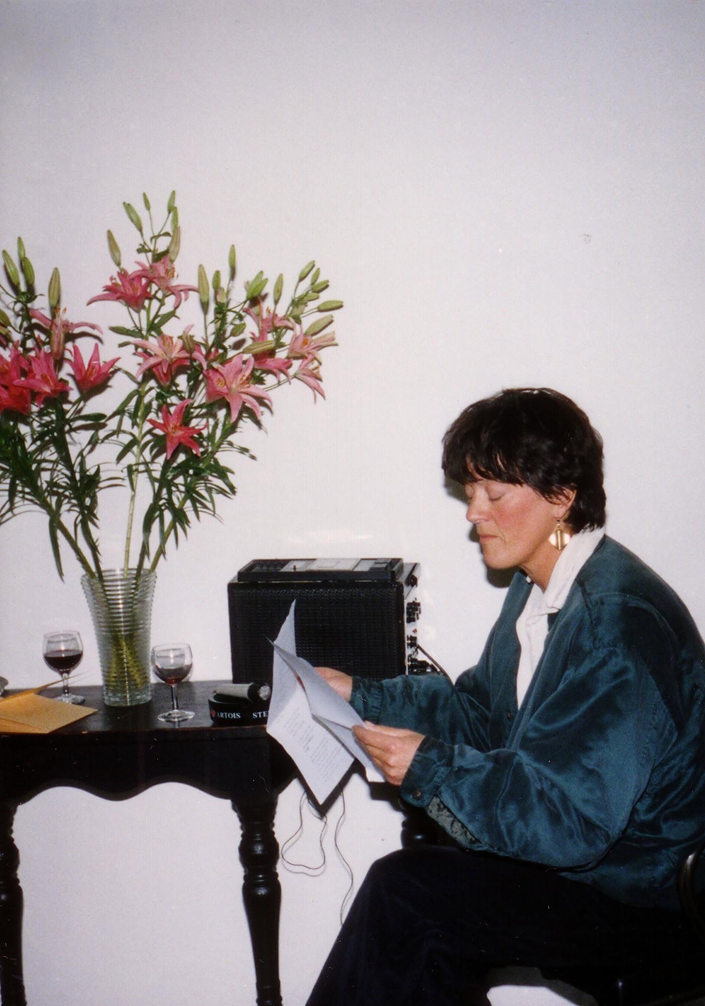 Rosalind Brackenbury reading from typewritten pages beside a cassette recorder and a vase of lilies