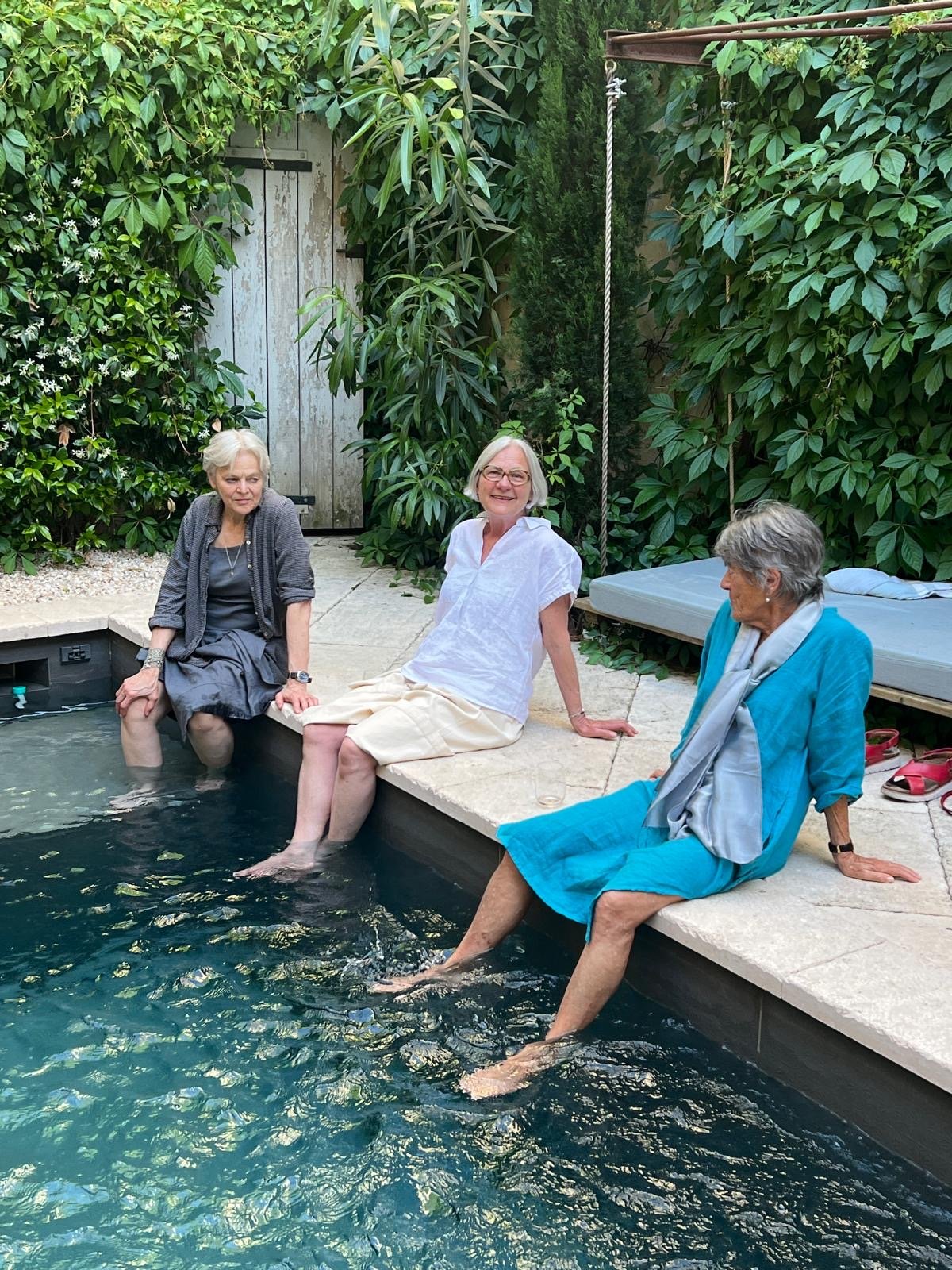 Three women sitting on the stone edge of the courtyard pool with their feet in the water